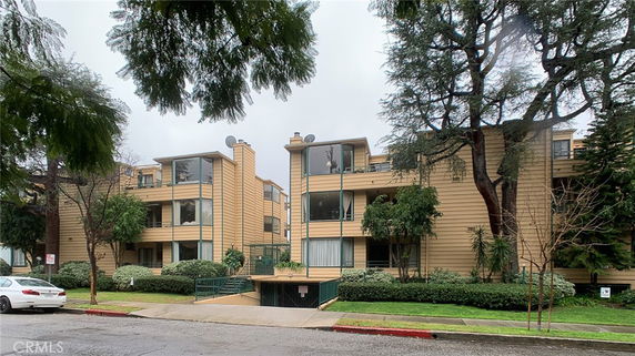 Front view of a multi-story residential building with balconies and surrounding trees.