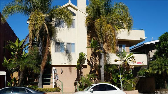 Front view of a multi-story building with balconies and surrounding palm trees.