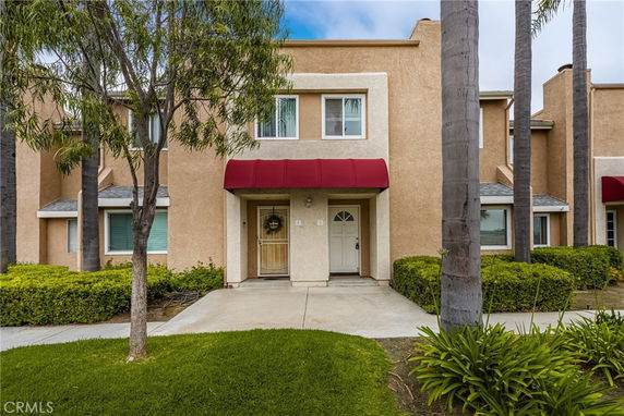 Front view of a two-story home with a red awning and a concrete walkway.