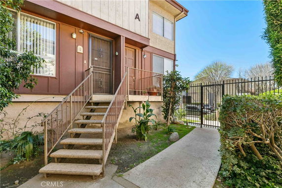 Front view of a two-story building entrance with stairs and a gated pathway.