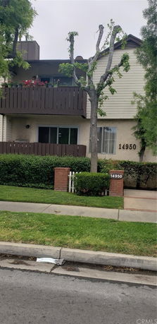 Front view of a two-story building with balconies and a tree in front.