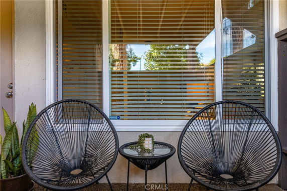 Outdoor seating area in front of a house window with blinds, featuring two black chairs and a small table.