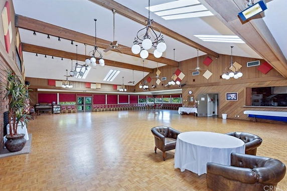 Large recreational room with wooden beams, chandeliers, and chairs along the wall.