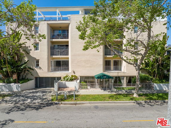Front view of a multi-story residential building with balconies and a green awning entrance.