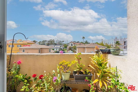 View from a balcony showing rooftops and plants, with suburban houses in the distance.