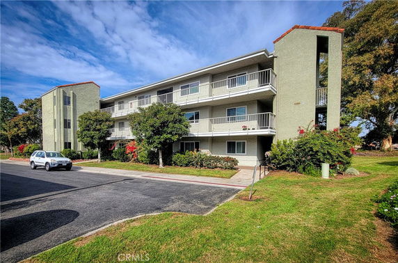 Front view of a three-story apartment building with balconies and a parking area.
