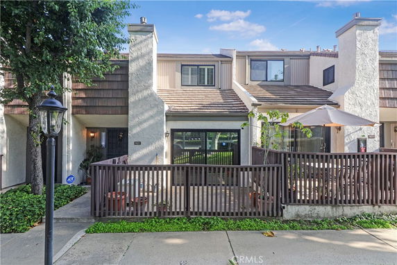 Front view of a two-story townhouse with a fenced patio and an umbrella.