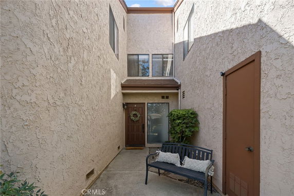 Front view of a two-story house with a narrow entrance and brown door, featuring a bench and small potted plant.