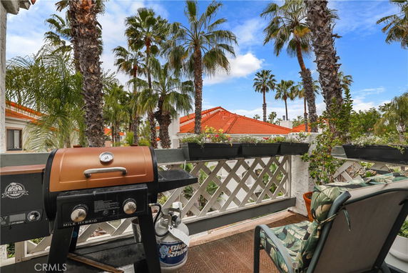 Rooftop patio with a barbecue grill and seating, surrounded by palm trees and red-tiled roofs.