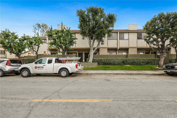 Front view of a multi-story residential building with trees and parked vehicles.