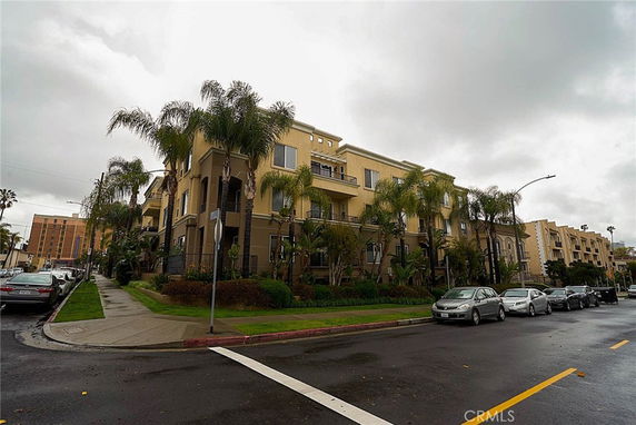 Front view of a multi-story apartment building with balconies and palm trees.