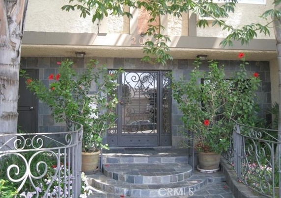Front view of a building entrance with a decorative metal gate and stone steps surrounded by plants.