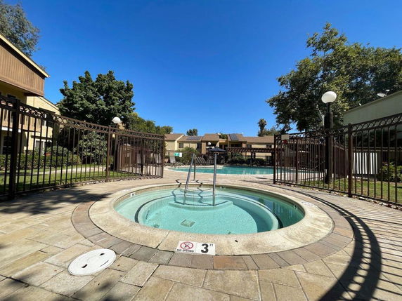 Outdoor swimming pool area with a hot tub and surrounding buildings.
