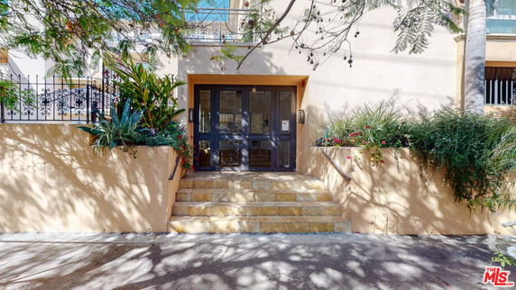 Front view of a building with stairs leading to the entrance, surrounded by plants.