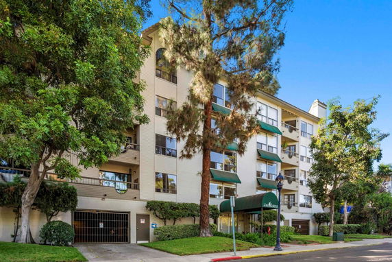 Front view of a multi-story residential building with balconies and green awnings.