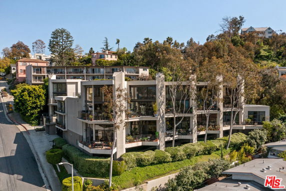 Front view of a multi-story apartment building with large balconies and surrounding trees.