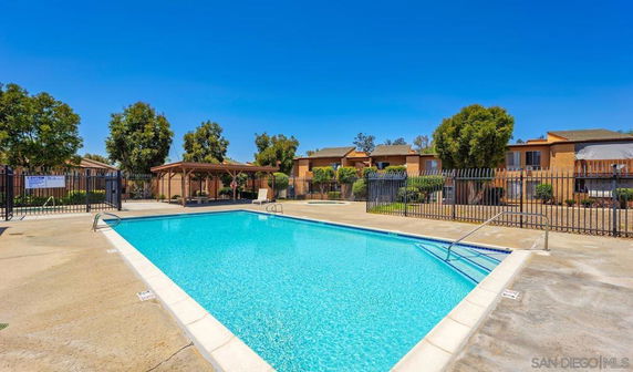 Outdoor swimming pool with surrounding fence and buildings in the background.