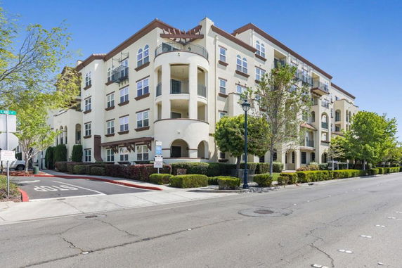 Front view of a multi-story residential building with balconies and landscaped surroundings.