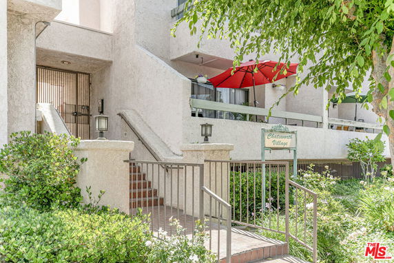Front view of a multi-story building with staircases and a red umbrella on the balcony.