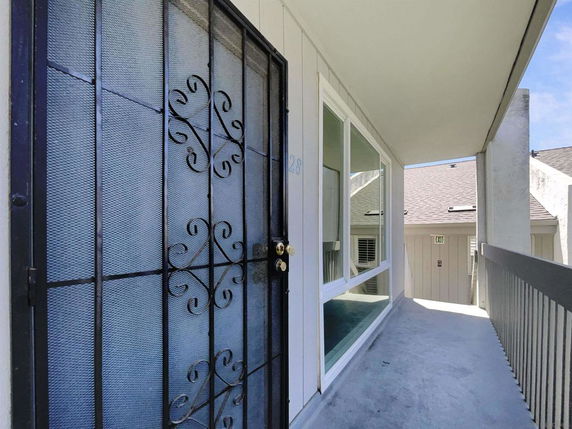 Exterior view of a building corridor with a decorative metal security door and windows.