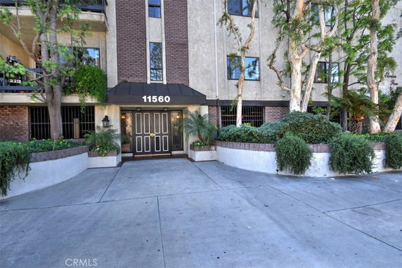 Front view of a multi-story building entrance with plants and trees.