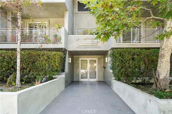Front view of a building entrance with balconies and surrounding greenery.