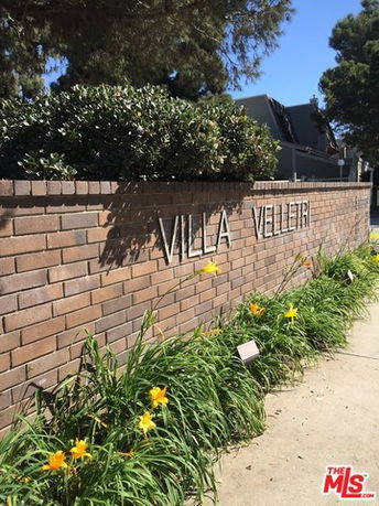 Front view of a brick wall with the name 'Villa Velletri' and surrounding plants.