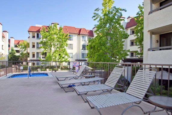 Outdoor area with a small swimming pool and lounge chairs, surrounded by multi-story buildings with red roofs.