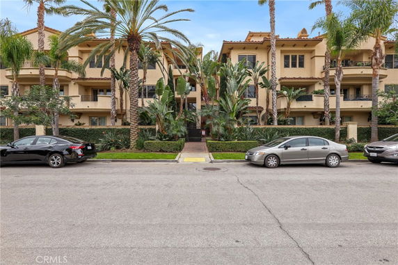 Front view of a multi-story residential building with balconies and palm trees.