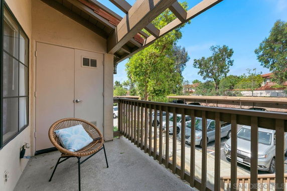 Balcony with a wicker chair overlooking a parking area and trees.