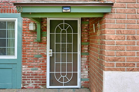 Front view of a house entrance with a decorative screened door and brick exterior.