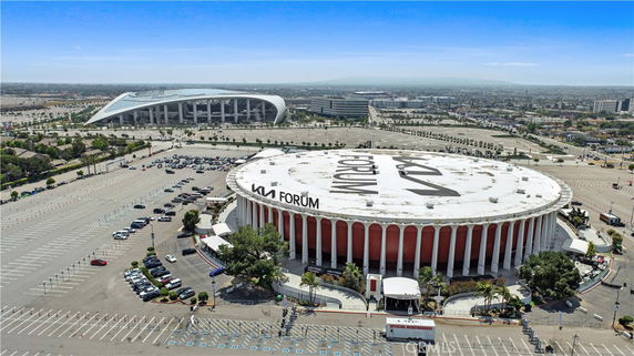 Aerial view of a round building with columns surrounded by a large parking area and another large structure in the background.