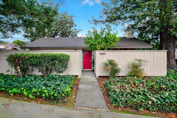 Front view of a single-story house with a red door and surrounding fence.