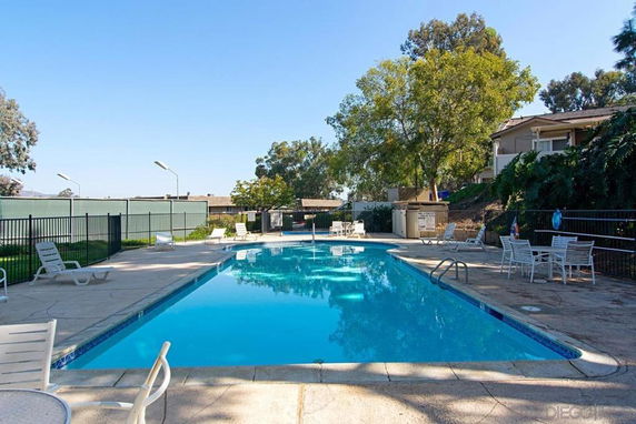 Outdoor swimming pool area with chairs and tables surrounding it.
