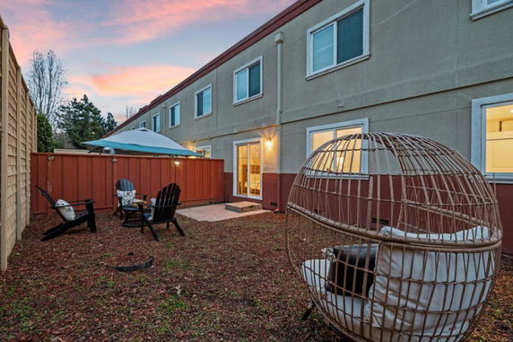 View of a two-story house with a backyard seating area featuring chairs and a wicker egg chair.