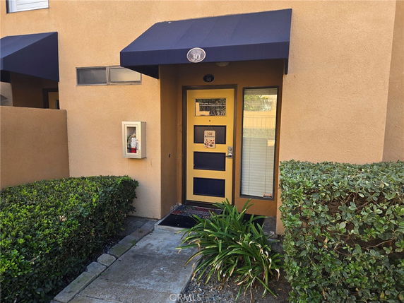 Front view of a house entrance with a blue awning and plants.
