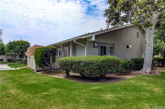 Front view of a single-story house with a patio umbrella and shrubs.