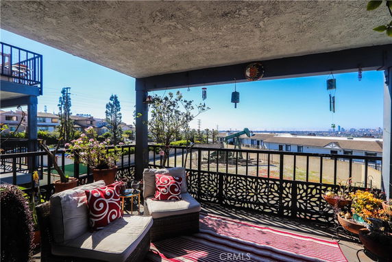 Covered outdoor patio area with seating, overlooking houses and a distant cityscape.