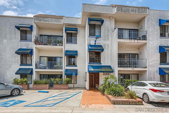 Front view of a multi-story building with balconies and blue awnings.