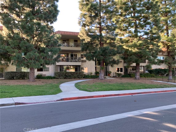 Front view of a multi-story residential building with balconies and surrounded by trees.
