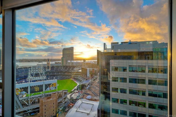 View of a cityscape with a stadium and tall buildings during sunset from a window.