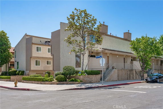 Front view of a multi-story residential building on a corner lot with stairs and landscaping.