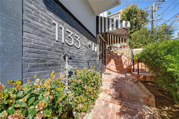 Front view of a house with a brick pathway and a striped awning.