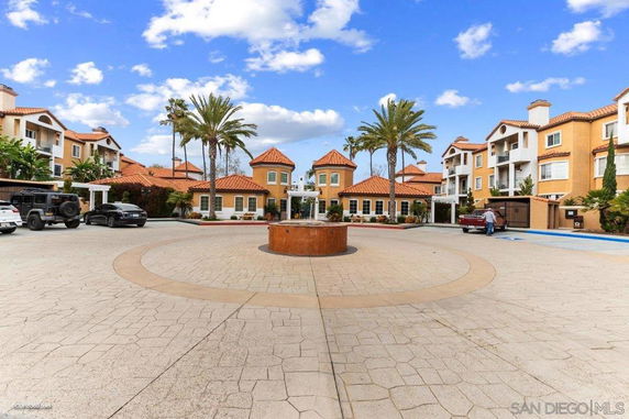 Front view of a multi-story residential complex with terracotta roofs and palm trees.