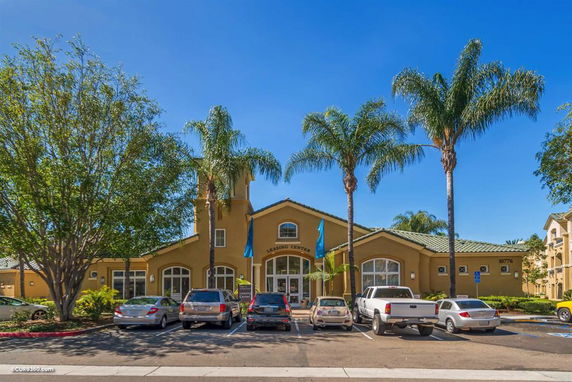 Front view of a building with palm trees in the foreground and multiple parked cars.