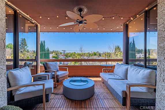 Seating area on a balcony with a view of surrounding trees and houses, decorated with string lights and a ceiling fan.