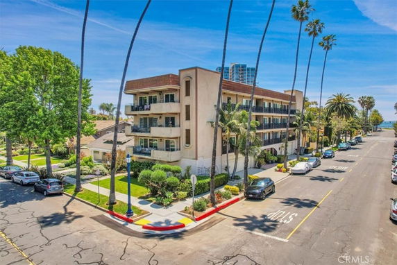 Front view of a multi-story building on a corner lot with balconies and palm trees.