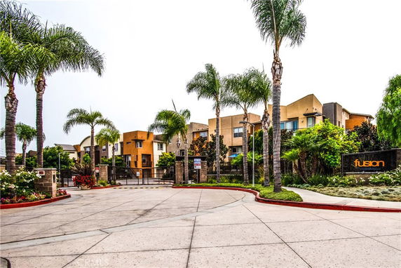 Front view of a gated residential complex with multiple buildings and palm trees.