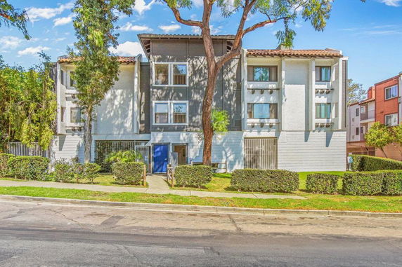 Front view of a three-story apartment building with trees and hedges.