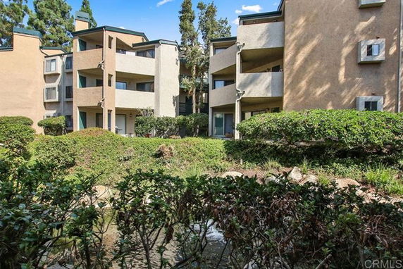 Front view of a multi-story apartment building with balconies and surrounding greenery.